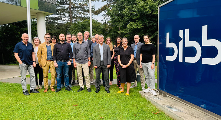 Gruppenfoto aller Teilnehmer vor dem BIBB-Gebäude neben dem Bibb-Glasaufsteller mit BIBB-Logo