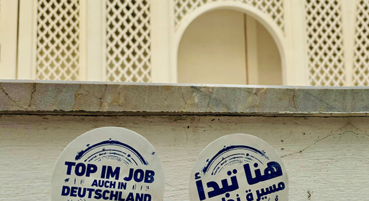 Bild einer Wand mit "Top im Job auch in Deutschland" Sticker in Deutsch und Arabisch