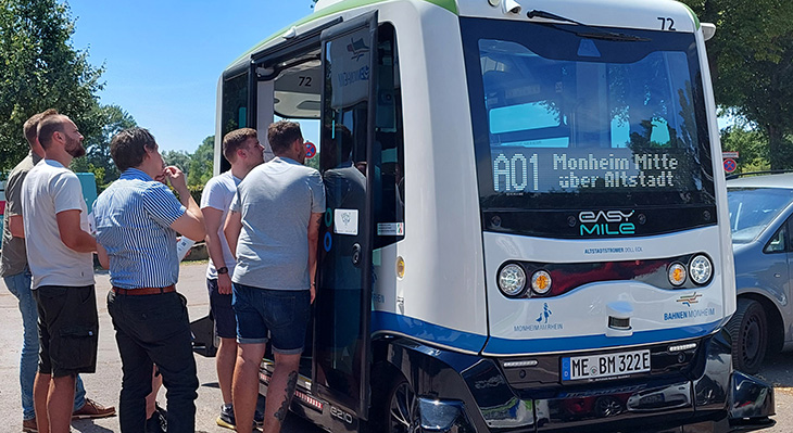 Ein autonom fahrendes Fahrzeug steht mit offenen Türen an einem Parkplatz und es steigen mehrere Personen ein.