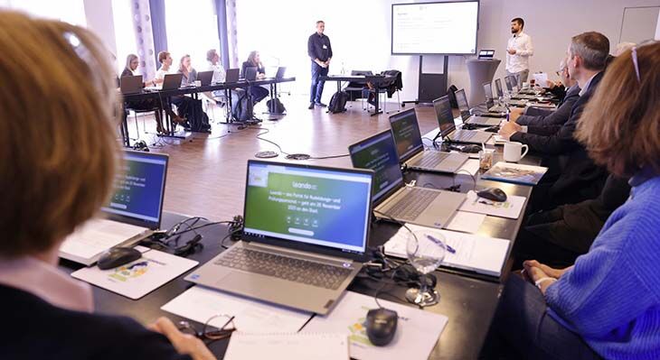 Worshop mit U-förmiger Bestuhlung und sitzenden Teilnehmern mit Laptops auf den Tischen