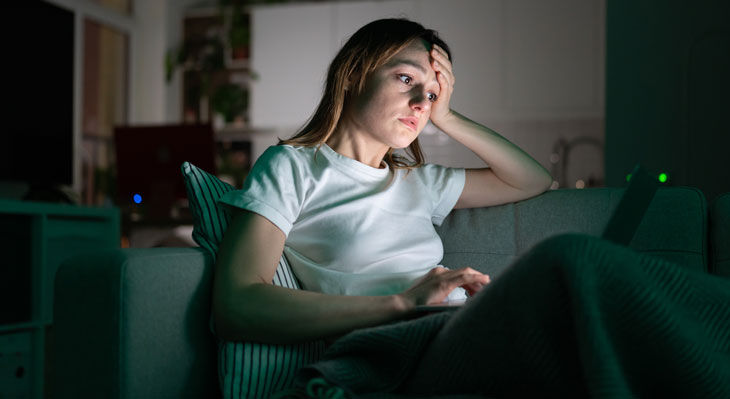 Erschöpfte Frau sitzt auf dem Sofa mit einem Laptop auf dem Schoß