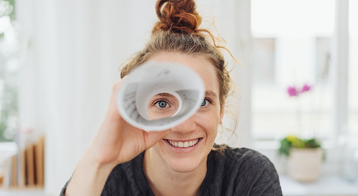 Eine junge Frau schaut durch ein Fernrohr aus Papier und lacht.