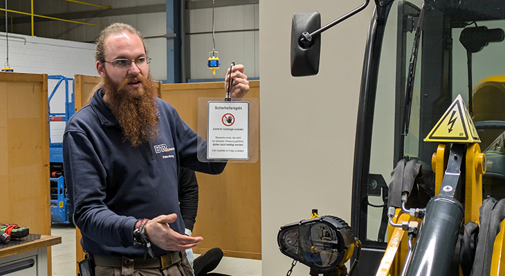 Ausbilder Fabio Ahring hält während eines Workshops zur Freischaltung eines Hochvolt-Systems ein Hinweisschild in der Hand.