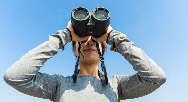 Frau schaut mit Fernglas in den blauen Himmel