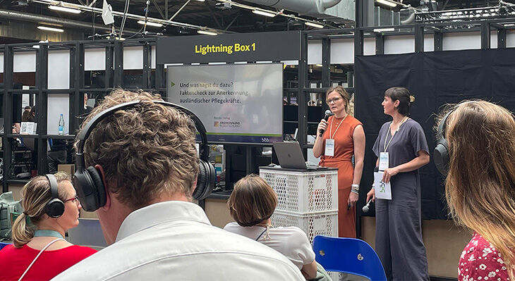 Ricarda Knöller / Mareike Freitag  stehen auf der Bühne. Im Vordergrund sieht man Zuschauer